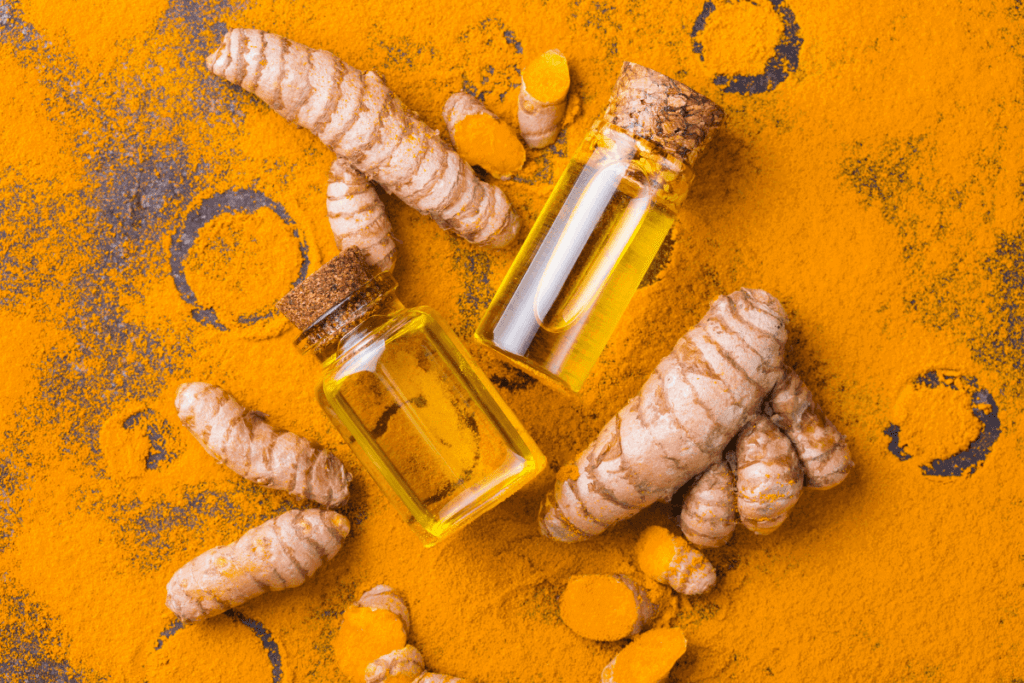turmeric root and bottles of oil on tumeric powder background