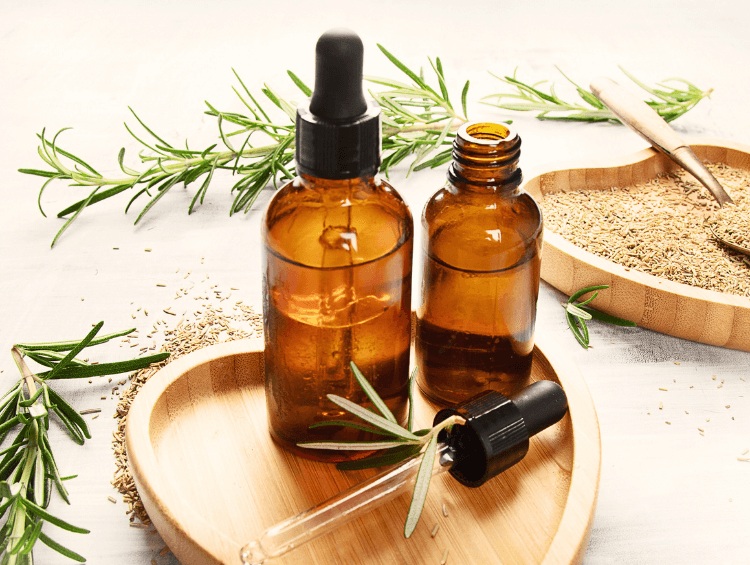 two amber bottles of rosemary oil, surrounded by fresh rosemary leaves