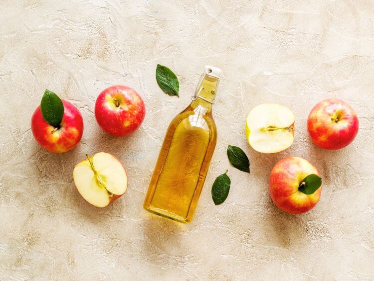 bottle of apple cider vinegar, surrounded by red apples