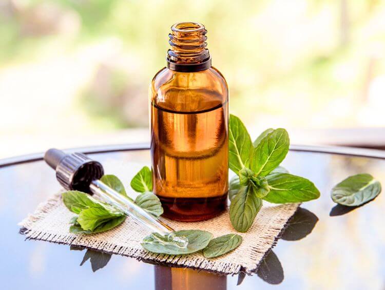 amber dropper bottle of hair oil, surrounded by peppermint leaves